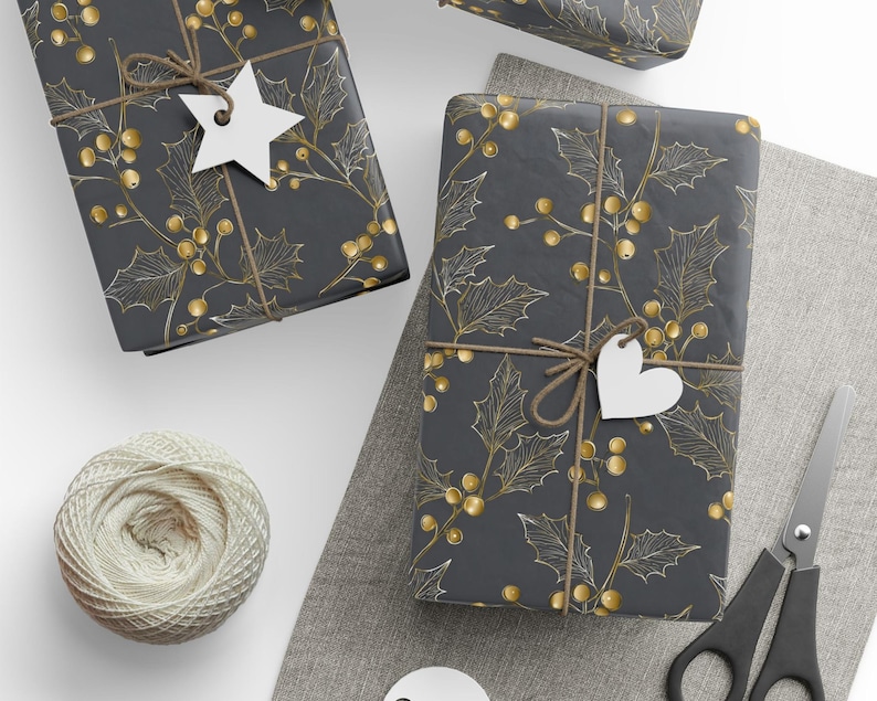 May include: Wrapped gifts with a dark gray background and a gold holly leaf and berry pattern. Each gift is tied with twine and has a white tag. A ball of twine, scissors, and a gray cloth are also in the image.