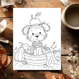 May include: A black and white line art illustration featuring a small, fluffy dog wearing a striped scarf, sitting inside a basket filled with pumpkins and apples. An apple rests on the dog's head. The text PIXELPETITESHOP appears at the top center.