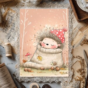 May include: A rectangular art print featuring a cartoon hedgehog with closed eyes wearing a red and white polka dot hat, nestled inside a beige knit pouch. The illustration includes a small mushroom, a snail, and scattered autumn leaves.