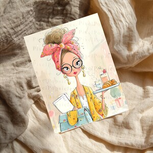May include: A rectangular art print featuring a stylized illustration of a person with a messy bun, a pink patterned headscarf, and round glasses. The person wears a yellow floral cardigan, carries a blue bag, and holds a tray with a drink and croissant.