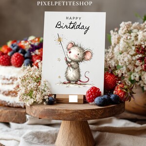 May include: A birthday card with a watercolor illustration of a mouse holding a sparkler, with the words "Happy Birthday" in elegant script. The card is displayed on a wooden stand, with a cake and berries in the background.