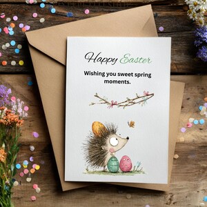 Pode incluir: Um cart&atilde;o de felicita&ccedil;&otilde;es de P&aacute;scoa com o texto "Happy Easter" e "Wishing you sweet spring moments." O cart&atilde;o apresenta uma ilustra&ccedil;&atilde;o de um ouri&ccedil;o com ovos de P&aacute;scoa e uma borboleta. Est&aacute; dentro de um envelope castanho, com confetes e flores espalhados.