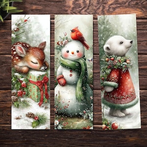 May include: Three Christmas bookmarks. One shows a sleeping fawn on a gift, another a snowman with a cardinal, and the last a polar bear in a red coat. Each has a snowy background with festive details, perfect for the holiday season.