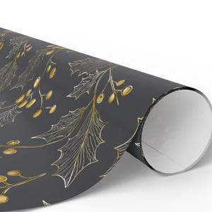 May include: A roll of wrapping paper with a repeating pattern of gold holly leaves and berries on a dark gray background. The paper is rolled up, revealing the white interior.