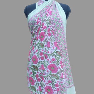 Op de afbeelding: Een groene en witte katoenen sarong met een roze bloemenprint. De sarong is om een ​​mannequin gewikkeld en heeft een rand met een ruitpatroon.