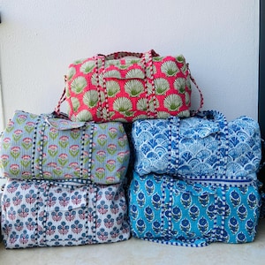 Puede incluir: Una pila de cinco bolsas de lona estampadas. La bolsa superior es rosa con un diseño de concha verde. Debajo hay bolsas con estampados florales azules, celeste y blancos. Cada bolsa tiene una correa y cierre de cremallera a juego.