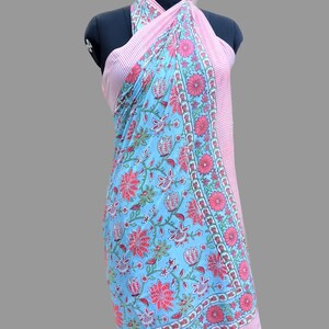 Op de afbeelding: Een lichtblauwe en roze sarong met een bloemenprint en een roze-witte gestreepte rand. De sarong is om een ​​mannequin gewikkeld en aan de nek gebonden.