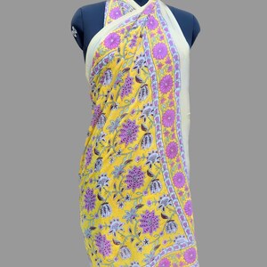 Op de afbeelding: Gele sarong met bloemenprint met roze en witte accenten. De sarong is gedrapeerd op een mannequin en is om de nek gebonden.