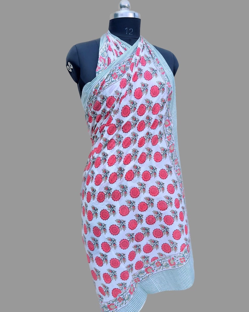 Op de afbeelding: Witte katoenen sarong met een rode bloemenprint. De sarong is om een ​​mannequin gebonden om te laten zien hoe hij als jurk gedragen kan worden.
