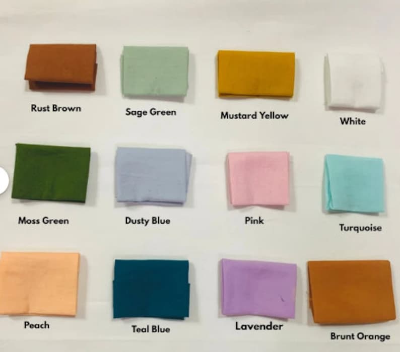 May include: An assortment of folded fabric swatches in various colors, including rust brown, sage green, mustard yellow, and white. Additional colors are moss green, dusty blue, pink, turquoise, peach, teal blue, lavender, and burnt orange. Each swatch has a color name printed below it.