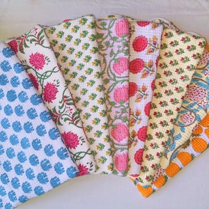 May include: A collection of colorful, patterned fabric squares. Designs include blue circles, pink flowers, green leaves, and orange strawberries. The fabrics are arranged in a fan shape, showcasing the variety of prints and colors.