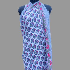 Op de afbeelding: Een blauwe en witte katoenen sarong met een bloemenprint. De sarong heeft een roze en groene rand met een gestreept patroon.
