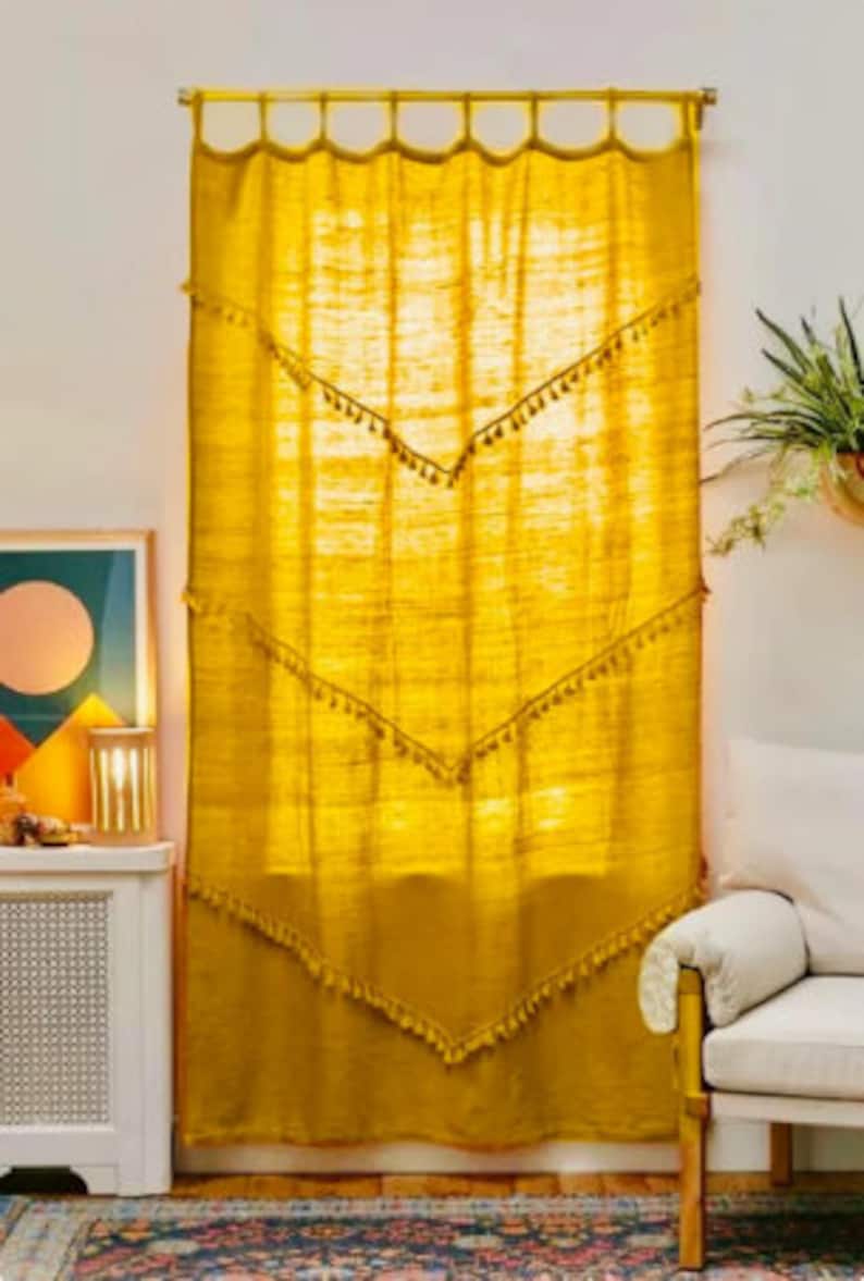 May include: Mustard yellow curtain with a textured weave, adorned with tassel trim along chevron-shaped seams. The curtain hangs from a scalloped rod, creating a warm, inviting ambiance. The curtain is a decorative window treatment.