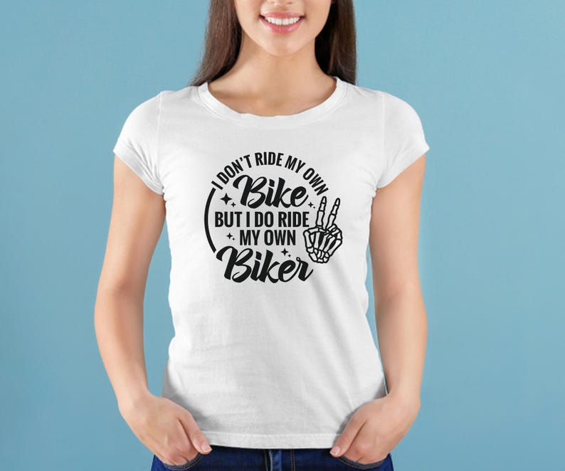 May include: White t-shirt with a black graphic that reads "I don't ride my own bike but I do ride my own biker" with a skeleton hand making a peace sign.