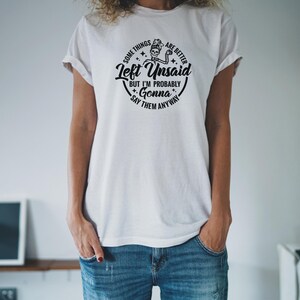May include: White t-shirt with a black graphic print of a skeleton holding a paintbrush and the text "Some things are better left unsaid but I'm probably gonna say them anyway".
