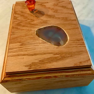 May include: A wooden box with a light brown finish. The box has a clear agate stone inlay and an orange crystal knob.