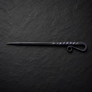 May include: A hand-forged metal letter opener with a dark charcoal gray finish. The tool features a long, tapered pointed blade and a handle designed with a twisted metal texture that ends in a decorative curled loop at the very base of the grip.