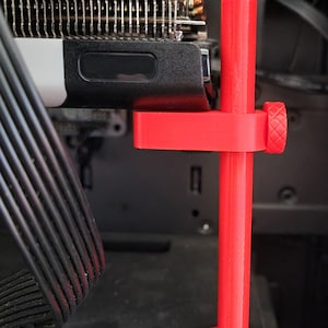 May include: A red 3D printed stand for a graphics card. The stand has a round base and a vertical support with a clamp at the top.