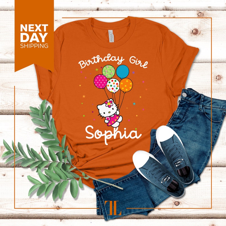 Puede incluir: Camiseta naranja con un gr&aacute;fico de Hello Kitty sosteniendo globos que dicen "Birthday Girl" y el nombre "Sophia".