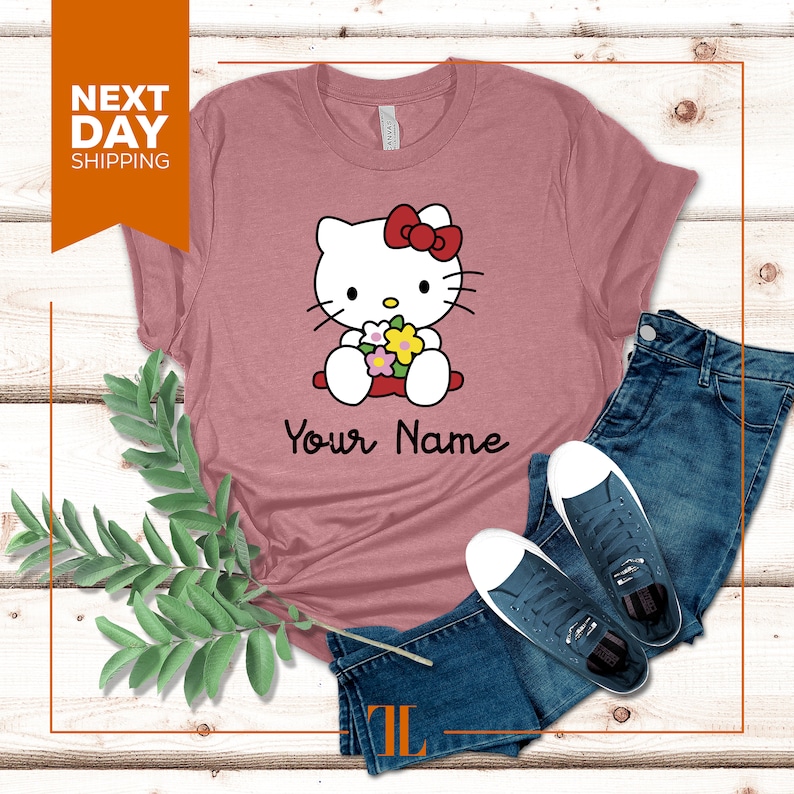 May include: A pink t-shirt with a cartoon image of Hello Kitty holding flowers. The text "Your Name" is printed below the image.