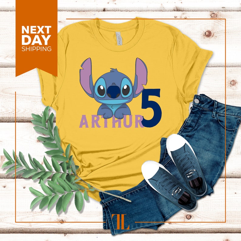 May include: Yellow t-shirt with a blue Stitch character from Lilo & Stitch, the number 5, and the name "Arthur" in purple lettering.