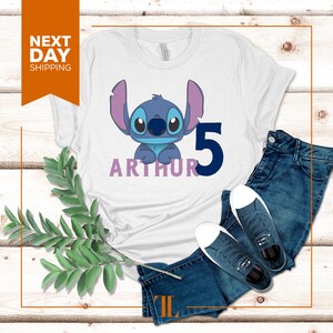 May include: White t-shirt with a blue Stitch character from Lilo & Stitch, the number 5, and the name Arthur in purple.