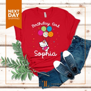 Puede incluir: Camiseta roja con un dise&ntilde;o blanco de Hello Kitty sosteniendo globos que dicen "Birthday Girl" y el nombre "Sophia" impreso debajo.
