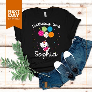 Puede incluir: Camiseta negra con un gr&aacute;fico blanco de un gato de dibujos animados sosteniendo globos que dicen "Birthday Girl" y el nombre "Sophia".