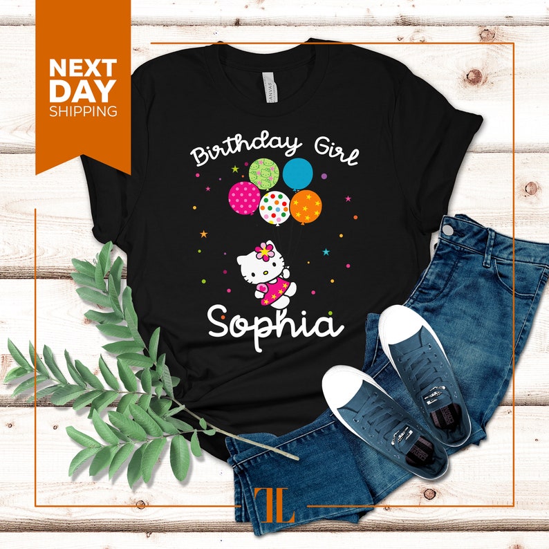 Puede incluir: Camiseta negra con un gr&aacute;fico blanco de un gato de dibujos animados sosteniendo globos que dicen "Birthday Girl" y el nombre "Sophia".