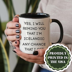 May include: A white ceramic mug with a black interior and handle, featuring the black printed text: YES, I WILL REMIND YOU THAT I'M ICELANDIC ANY CHANCE THAT I GET. A green scalloped badge with the text PROUDLY PRINTED IN THE USA is visible.