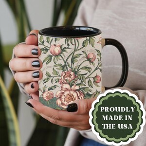 May include: A ceramic mug with a black interior and handle, featuring a floral design of pink peonies and green leaves on a cream background. The mug has the text "FUCK TULIP" and a green and white sticker that says "PROUDLY MADE IN THE USA".