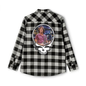 May include: Black and gray plaid button-down shirt. The back of the shirt features a white skull graphic with a photo of a man playing a guitar. The man is wearing a purple shirt.