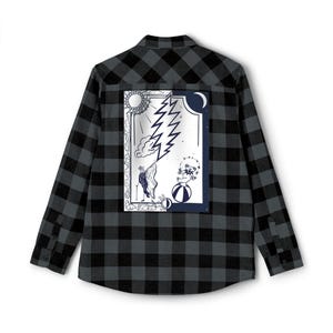 May include: A long-sleeved, button-down flannel shirt in a black and gray plaid pattern. The back of the shirt features a framed graphic with a sun, lightning bolt, moon, and a bear on a ball. The graphic is in black and white.