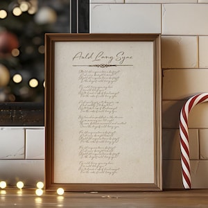 Puede incluir: Una impresión enmarcada de la letra de la canción "Auld Lang Syne" con un fondo de madera rústico. La impresión está en un marco marrón y está rodeada de una corona navideña, un bastón de caramelo y una vela blanca.