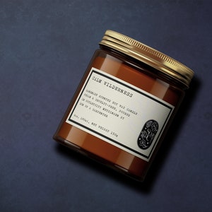 以下が含まれることがあります： 金色の蓋が付いた茶色のガラス製のキャンドルジャー。ラベルには「Calm Wilderness」と書いてあり、手作りの大豆ワックスキャンドルで、ウッディな香りがすると説明されています。キャンドルは6オンスで、重さは150gです。