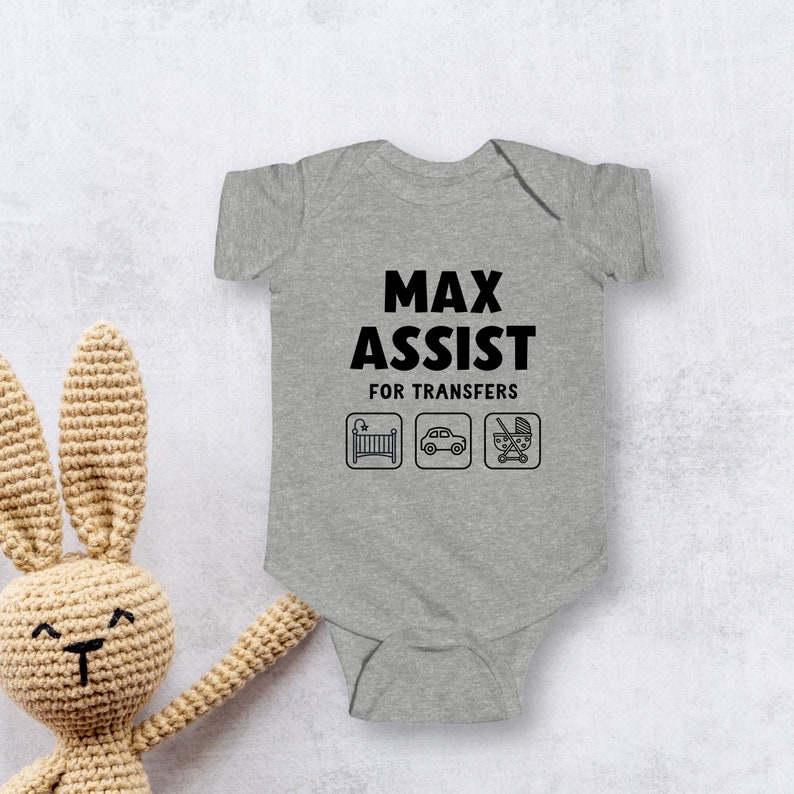 Może przedstawiać: Szary śpioszek dla niemowlęcia z napisem "Max Assist for Transfers" i trzema ikonami: ł&oacute;żeczkiem, samochodem i w&oacute;zkiem.