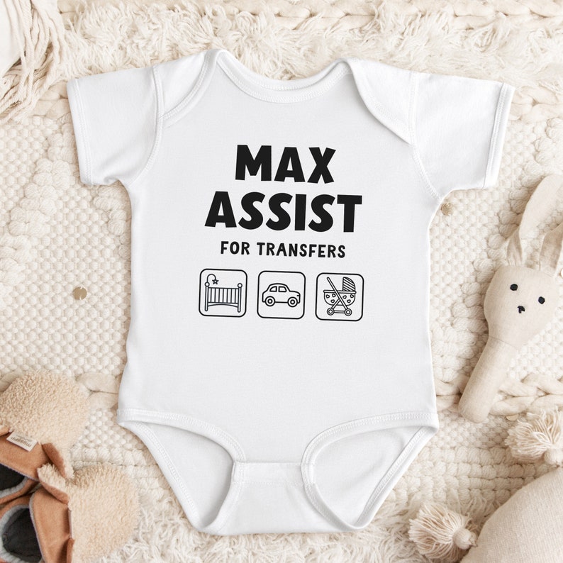 Może przedstawiać: Biały śpioszek dla niemowlęcia z czarnym napisem "Max Assist for Transfers" i trzema ikonami: ł&oacute;żeczkiem, samochodem i w&oacute;zkiem.