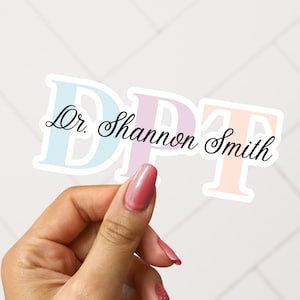 May include: A sticker with the letters "DPT" in pastel blue, pink, and peach colors. The sticker also includes the text "Dr. Shannon Smith" in black cursive writing.