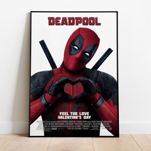 Puede incluir: Un p&oacute;ster enmarcado con Deadpool con un traje rojo y negro, formando un coraz&oacute;n con sus manos. El p&oacute;ster tiene la palabra "DEADPOOL" en rojo en la parte superior y el texto "FEEL THE LOVE VALENTINE'S DAY" en la parte inferior.