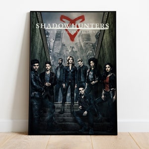May include: A poster for the TV show "Shadowhunters: The Mortal Instruments". The poster features a group of young adults standing on a set of stairs in a dark, urban setting. The show's title is displayed in large, white letters at the top of the poster, with the tagline "The Mortal Instruments" below it. A red rune symbol is prominently displayed in the center of the poster.