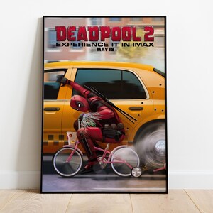 Puede incluir: Un p&oacute;ster enmarcado de la pel&iacute;cula Deadpool 2. El p&oacute;ster muestra a Deadpool montando una bicicleta rosa frente a un taxi amarillo. El t&iacute;tulo de la pel&iacute;cula y la fecha de estreno se muestran en la parte superior.