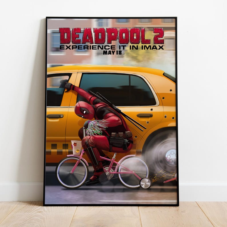 Puede incluir: Un p&oacute;ster enmarcado de la pel&iacute;cula Deadpool 2. El p&oacute;ster muestra a Deadpool montando una bicicleta rosa frente a un taxi amarillo. El t&iacute;tulo de la pel&iacute;cula y la fecha de estreno se muestran en la parte superior.
