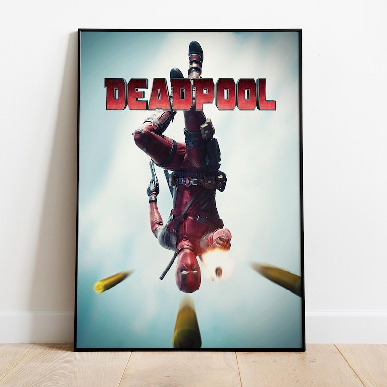 Puede incluir: Un p&oacute;ster enmarcado con el personaje Deadpool con un traje rojo y negro, boca abajo y sosteniendo una pistola. La palabra "DEADPOOL" est&aacute; en letras rojas en la parte superior. El fondo es un cielo azul claro con balas.