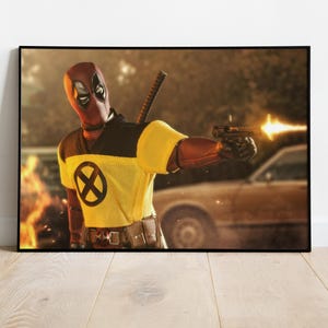 Puede incluir: Impresi&oacute;n enmarcada de un personaje con m&aacute;scara y traje rojo y negro, sosteniendo un arma con un destello de boca. El personaje lleva una camisa amarilla con un s&iacute;mbolo X negro. Una espada est&aacute; en la espalda del personaje.