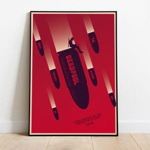 Puede incluir: Un p&oacute;ster enmarcado con un fondo rojo que presenta una ilustraci&oacute;n estilizada. Una figura est&aacute; sentada encima de una gran bala etiquetada como "Deadpool". Tambi&eacute;n hay varias otras balas con texto como "Wait", "You Get" y "A Load".