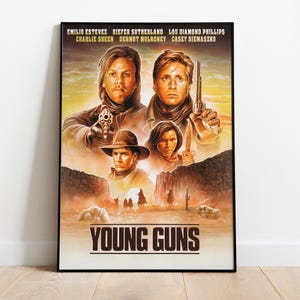 以下が含まれることがあります： 映画「ヤングガン」の額入りポスター。エミリオ・エステベス、キーファー・サザーランド、ルー・ダイアモンド・フィリップス、チャーリー・シーン、ダーモット・マローニー、ケイシー・シーマズコの肖像画が描かれています。砂漠の風景の中でリボルバーを持つ人物が描かれたアートワークです。