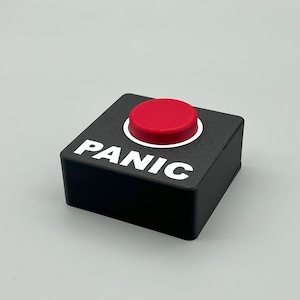 Może przedstawiać: Czarny kwadratowy przycisk z napisem "PANIC" w białym tekście. Przycisk ma czerwony okrągły wierzch z białym obramowaniem. Jest to przedmiot nowości.