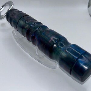 May include: A bottle opener featuring a cylindrical handle with a marbled, multi-coloured finish in shades of deep blue, purple, and black. The handle has a series of rounded ridges along its length, and the metal opener end is circular and silver.