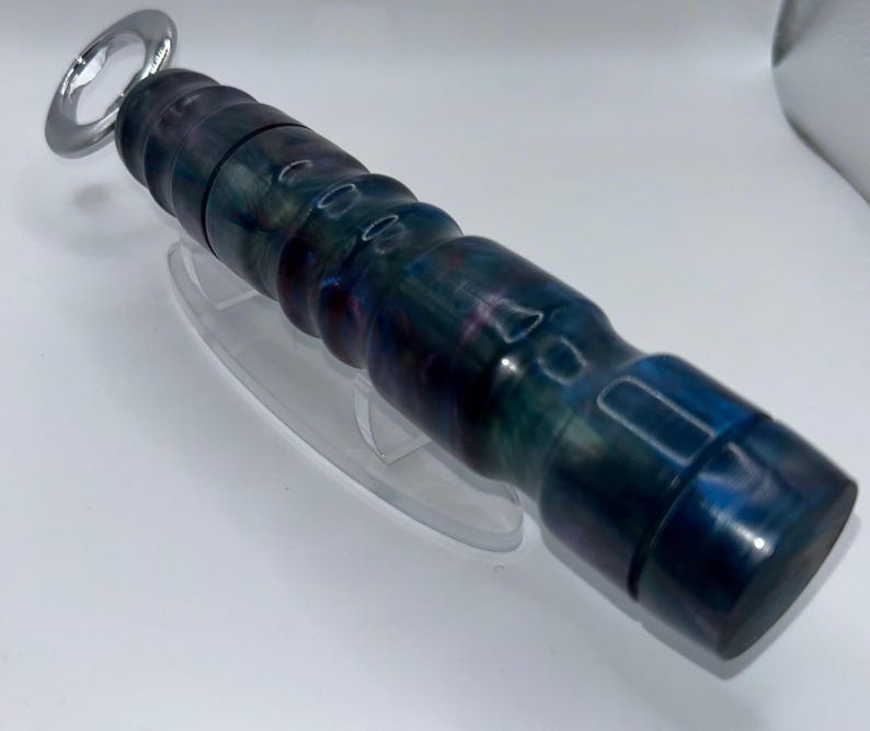 May include: A bottle opener featuring a cylindrical handle with a marbled, multi-coloured finish in shades of deep blue, purple, and black. The handle has a series of rounded ridges along its length, and the metal opener end is circular and silver.