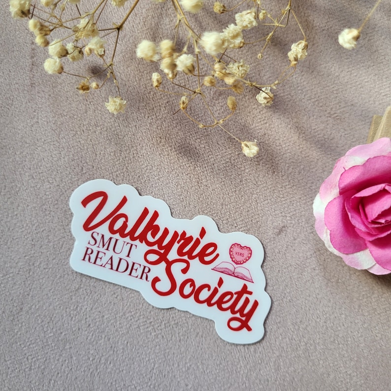 May include: White sticker with red text that reads "Valkyrie Smut Reader Society" with a red heart and open book graphic.